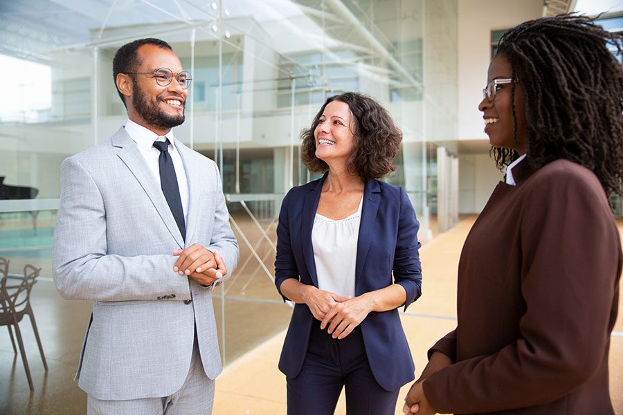 Business Insurance - View of Diverse Group of Smiling Employees Standing in a Modern Office Building Talking to Each Other