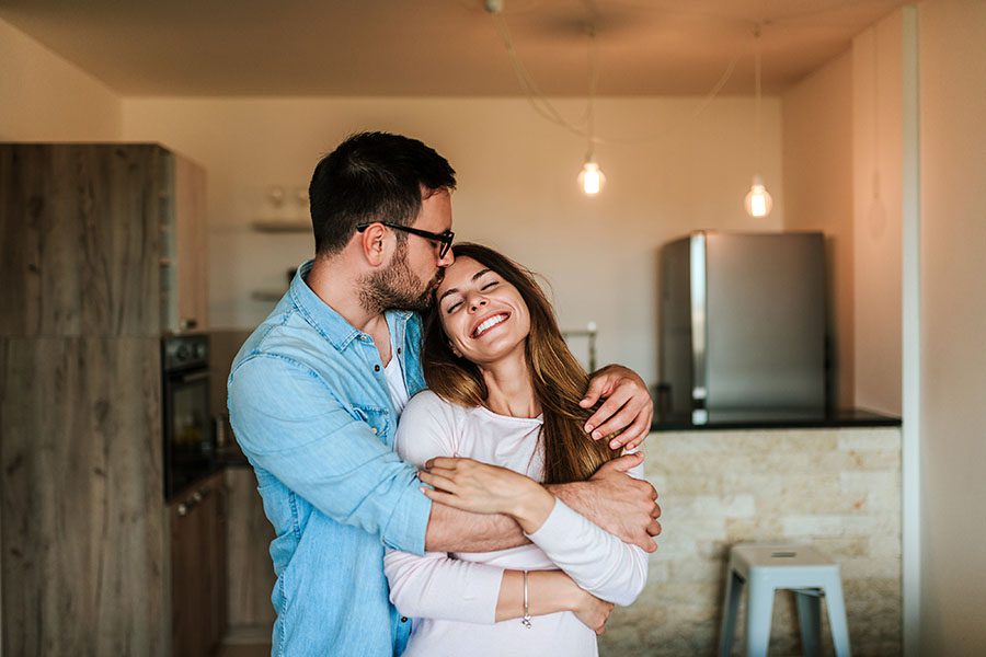 Personal Insurance - Portrait of a Cheerful Young Couple Hugging Each Other in Their New Apartment